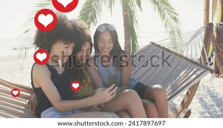 Image of red heart love digital icons over female friends in hammock with smartphone on beach. digital interface, social media and global networking concept digitally generated image.