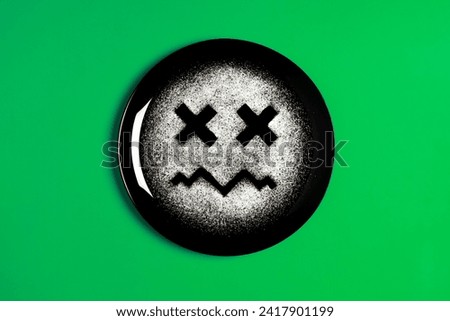 Sad face, face I don't like, concept made with plate and flour, green background, x-shaped eyes, black plate, sad mood, facial expressions