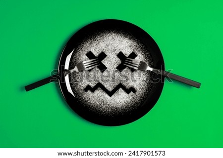 Sad face, face I don't like, concept made with plate and flour, green background, x-shaped eyes, black plate, sad mood, facial expressions, forks in the shape of arms with different positions