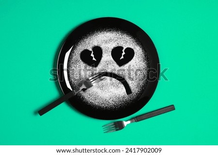 Sad face, face I don't like, concept made with plate and flour, light green background, heart shaped eyes, black plate, sad mood, facial expressions