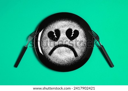 Sad face, face I don't like, concept made with plate and flour, light green background, heart shaped eyes, black plate, sad mood, facial expressions, forks in the shape of arms with different position