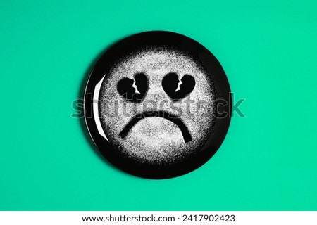 Sad face, face I don't like, concept made with plate and flour, light green background, heart shaped eyes, black plate, sad mood, facial expressions, forks in the shape of arms with different position