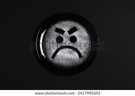 Displeased face, frowning eyebrows, concept made with plate and flour, black background, black plate, sad mood, facial expressions