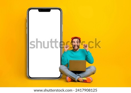 Full size photo of lucky guy wear teal sweatshirt sit with laptop near screen empty space win lottery isolated on yellow color background