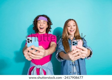 Photo of positive two teenagers takes pictures themselves holding new iphone 15 creating content isolated over aquamarine color background
