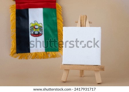 Empty white paper board template National symbol of UAE. United Arab Emirates small flag with Peregrine falcon on neutral beige background. Copy space for your text. Concept of Independence  Royalty-Free Stock Photo #2417931717