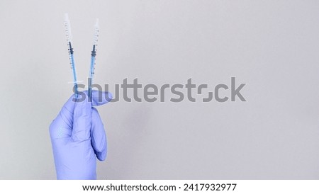 Hand in blue gloves of doctor or nurse holding syringe with liquid vaccine over grey background with copy space. New vaccine. Unknown vaccine. Medical gloves.