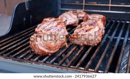Grilled meat steak wrapped in bacon on stainless BBQ grill with flames on dark background. Food and cuisine concept.