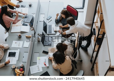 Multicultural coworkers collaborate in a modern office lobby, using technology to achieve tasks and discuss project solutions. Royalty-Free Stock Photo #2417940645