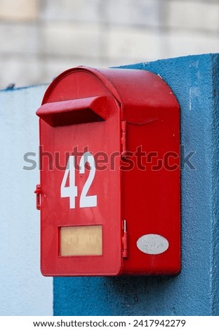 A red mail box sitting on top of a blue wall