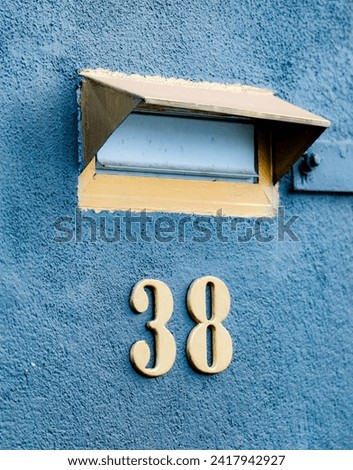 A letter box with number 38 sitting on the side of a blue wall