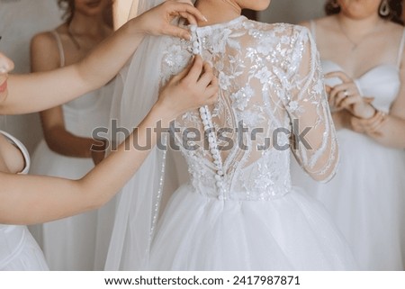 Wedding morning. Bridesmaids help put on the white wedding dress. A young woman is preparing to meet her groom and having fun with her friends Royalty-Free Stock Photo #2417987871