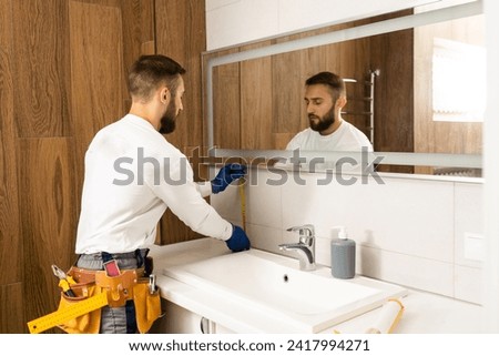 The worker installs the mirror in the bathroom. Royalty-Free Stock Photo #2417994271