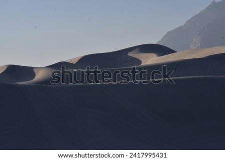 Desert dunes patterns and shadows Mountain and sky in background 