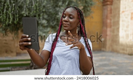 Beautiful african american woman brimming with confidence, smiling joyfully while having an enjoyable and fun video call on her gadget at a city street under the warm urban sunlight