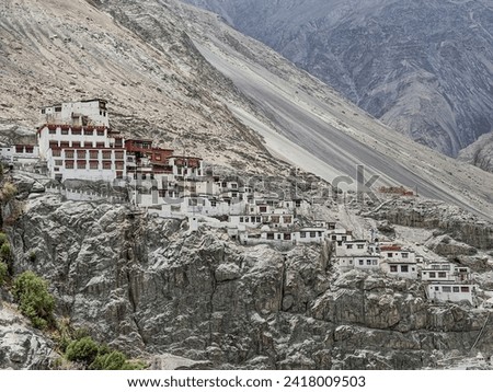 A serene view of a cliffside Buddhist monastery in the Himalayas, integrating historical architecture with the raw beauty of the Nubra Valley's rugged landscape.