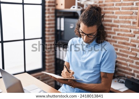 Young hispanic man business worker writing on notebook at office