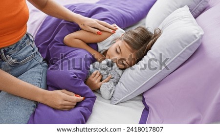 A woman comforts a sleeping girl with a stuffed animal in a cozy bedroom, depicting a tender family moment. Royalty-Free Stock Photo #2418017807