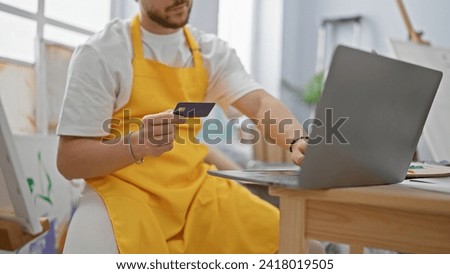 Young hispanic man artist shopping with credit card and laptop at art studio