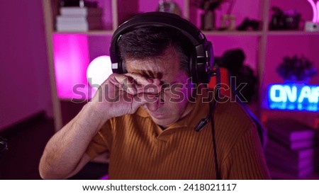 Stressed middle-aged man with headphones in dark gaming room looks tired