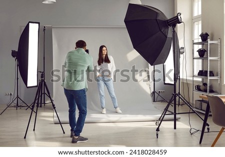 Beautiful model posing for male photographer in studio. Rare view of photographer taking pictures of female model with digital camera in photo studio with professional photographic equipment