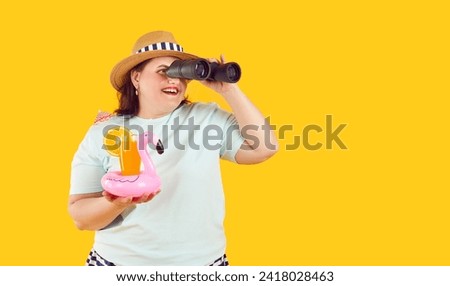 Excited plus size woman tourist looking through binoculars. Portrait of cheerful young woman with tropical cocktail standing on isolated studio background. Summer vacation, preparing for traveling Royalty-Free Stock Photo #2418028463