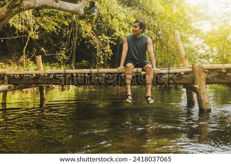 Man sitting on a wooden bridge in a natural waterfall place Royalty-Free Stock Photo #2418037065