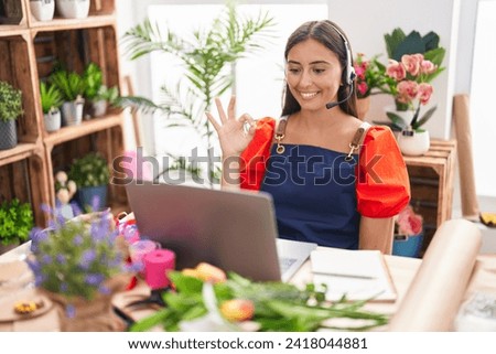 Young hispanic woman working at florist shop doing video call doing ok sign with fingers, smiling friendly gesturing excellent symbol 