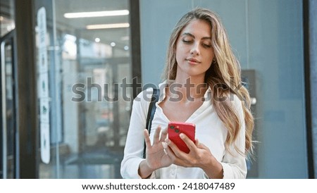 Attractive young blonde woman seriously engrossed in her cellphone, standing coolly on a sunny, urban street, with a relaxed concentration that's all about today's digital lifestyle. Royalty-Free Stock Photo #2418047489