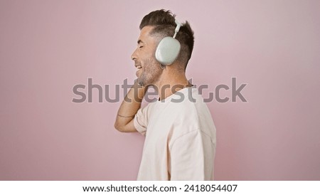 Young hispanic man listening to music singing song over isolated pink background