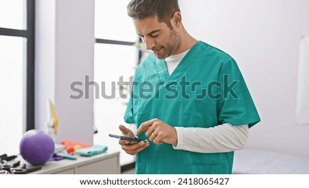 Hispanic male nurse in scrubs using smartphone at rehab clinic.