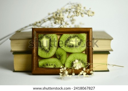 sliced ​​kiwi in a wooden frame on a white background and books nearby