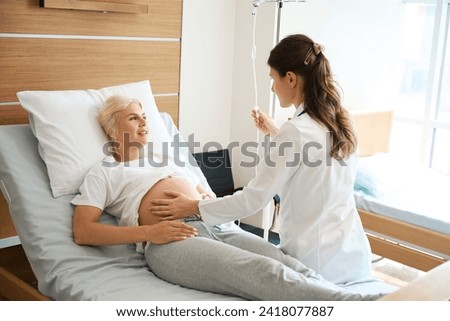 Woman looking at doctor checking her pregnant belly and put drop counter
