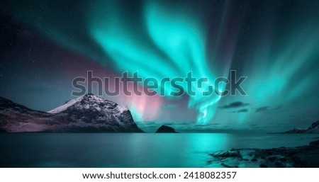 Northern Lights over the sea, snowy mountains at starry winter night. Aurora borealis in Lofoten islands, Norway. Sky with polar lights. Landscape with aurora, beach, sky, reflection in water. Space