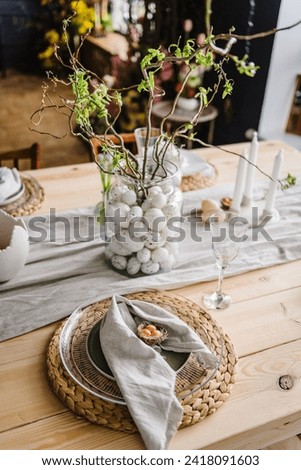 Setting table for Easter dinner with candle, ceramic plates with easter eggs in nest, bunny made of linen napkin. Holidays celebration concept. Decor with vase with twig, branch, leave at home. Set up