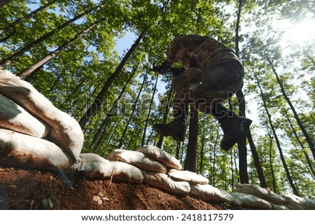 An elite soldier adeptly clears military barriers in the perilous wooded terrain, showcasing tactical skill and agility during specialized training Royalty-Free Stock Photo #2418117579