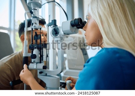 Female ophthalmologist using optical instrument while examining eye sight of a man at the clinic. Royalty-Free Stock Photo #2418125087