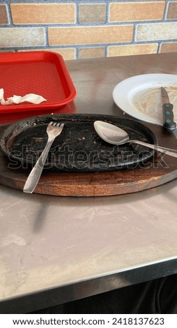 A finished black hot plate with a fork and spoon on top and several plates