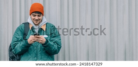 young man with mobile phone on outdoor wall background wearing winter clothes