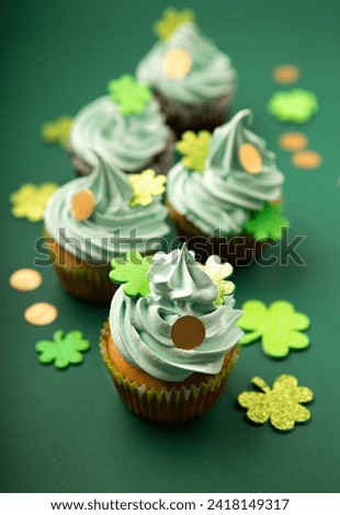 St. Patrick's Day vanilla and chocolate cupcakes with green frosting and  shiny clover decorations on green paper background. Irish holiday dessert concept, copy space. 