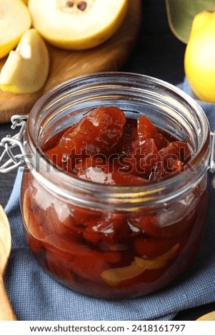 Quince jam in glass jar and fresh raw fruits on table, closeup