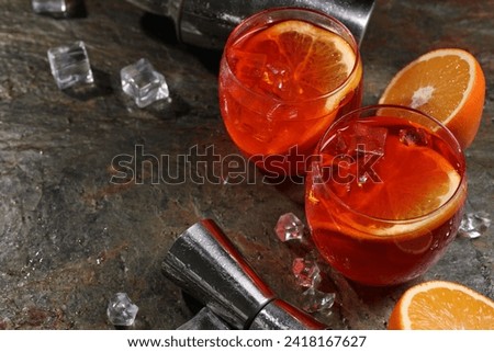 Aperol spritz cocktail, ice cubes and orange slices in glasses on grey textured table, space for text
