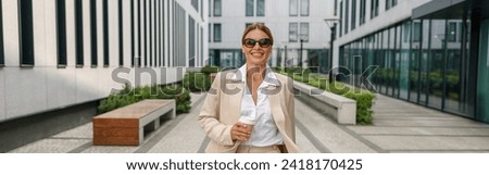 Smiling business woman with coffee walking on modern building background during break time
