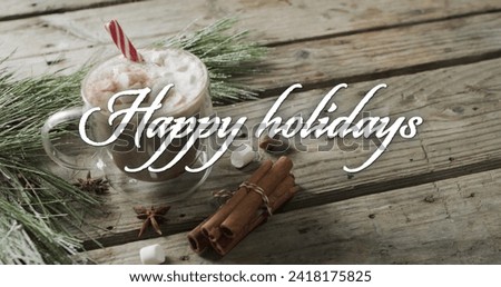 Happy holidays text in white over christmas hot chocolate and cinnamon sticks on wooden background. Christmas, tradition, greetings and celebration digitally generated image.
