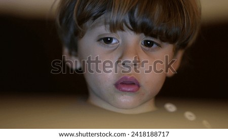 Closeup face watching cartoons hypnotized by online content. Child staring at entertainment media with blank expression, Childhood tech addiction concept