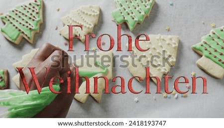 Frohe weihnachten text in red over caucasian hand decorating christmas cookies on white background. Christmas, tradition, german, greetings and celebration digitally generated image.