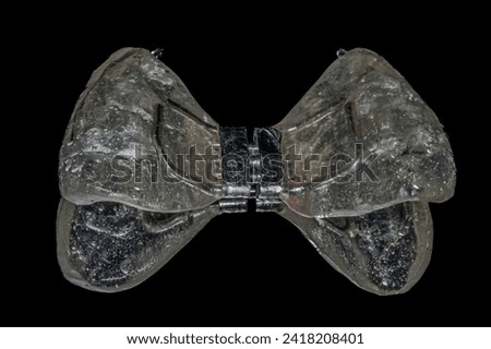 Palatal expander device to widen the upper jaw or maxilla in orthodontics treatment in transparent acrylic resin with metal hooks and a check actuator. Isolated in black background mirror reflection.
