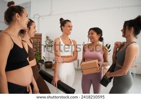 Diverse group of girls smiling happily in sportswear talking standing holding personal mats wait for yoga session. Cheerful female friends working out together in a fitness studio. Sorority. Royalty-Free Stock Photo #2418210595