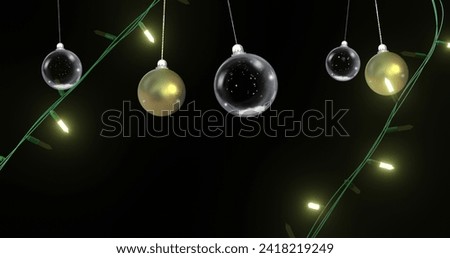 Yellow christmas string lights flashing over swinging gold and clear baubles on black background. Christmas, decorations, tradition and celebration digitally generated image.