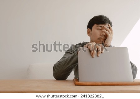 Asian man feeling bored tired and sleepy working with computer.
